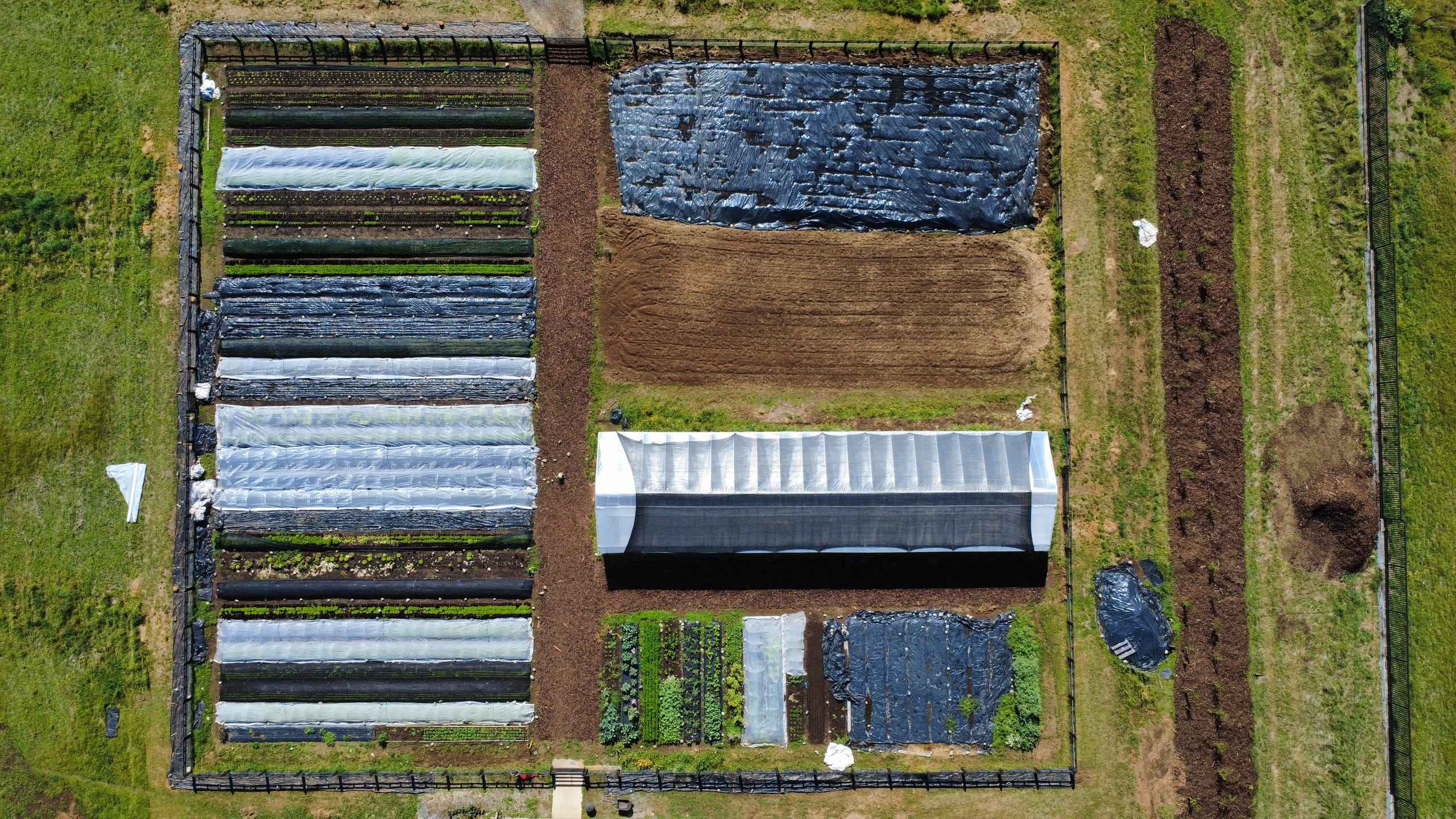 Vista aérea del Huerto Ñancul: hileras de cultivos, invernaderos y compost rodeados de bosque